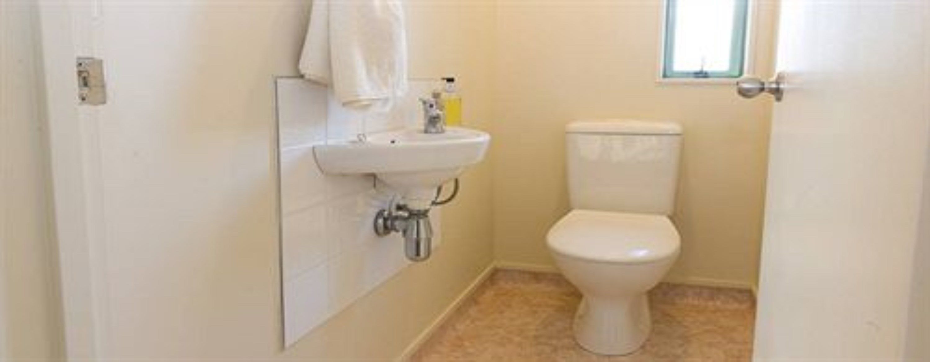 A small, clean bathroom with a white sink, toilet, and a small window.