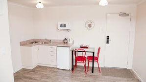 A small kitchen with a sink, microwave, and a small refrigerator. There is a dining table with two red chairs and a clock on the wall. - Hamilton Settlers Motor Lodge (Hamilton)