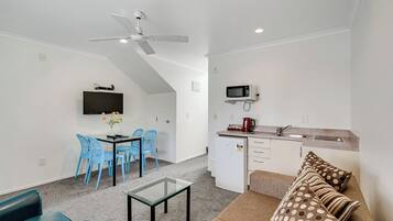 Un espacio habitable compacto con kitchenette, una zona de comedor con sillas azules, un sofá con cojines estampados y un ventilador de techo.