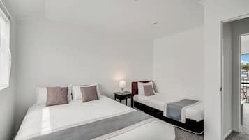 Quarto de hotel com uma cama grande, uma cama menor, mesa de cabeceira com luminária e vista para o exterior.