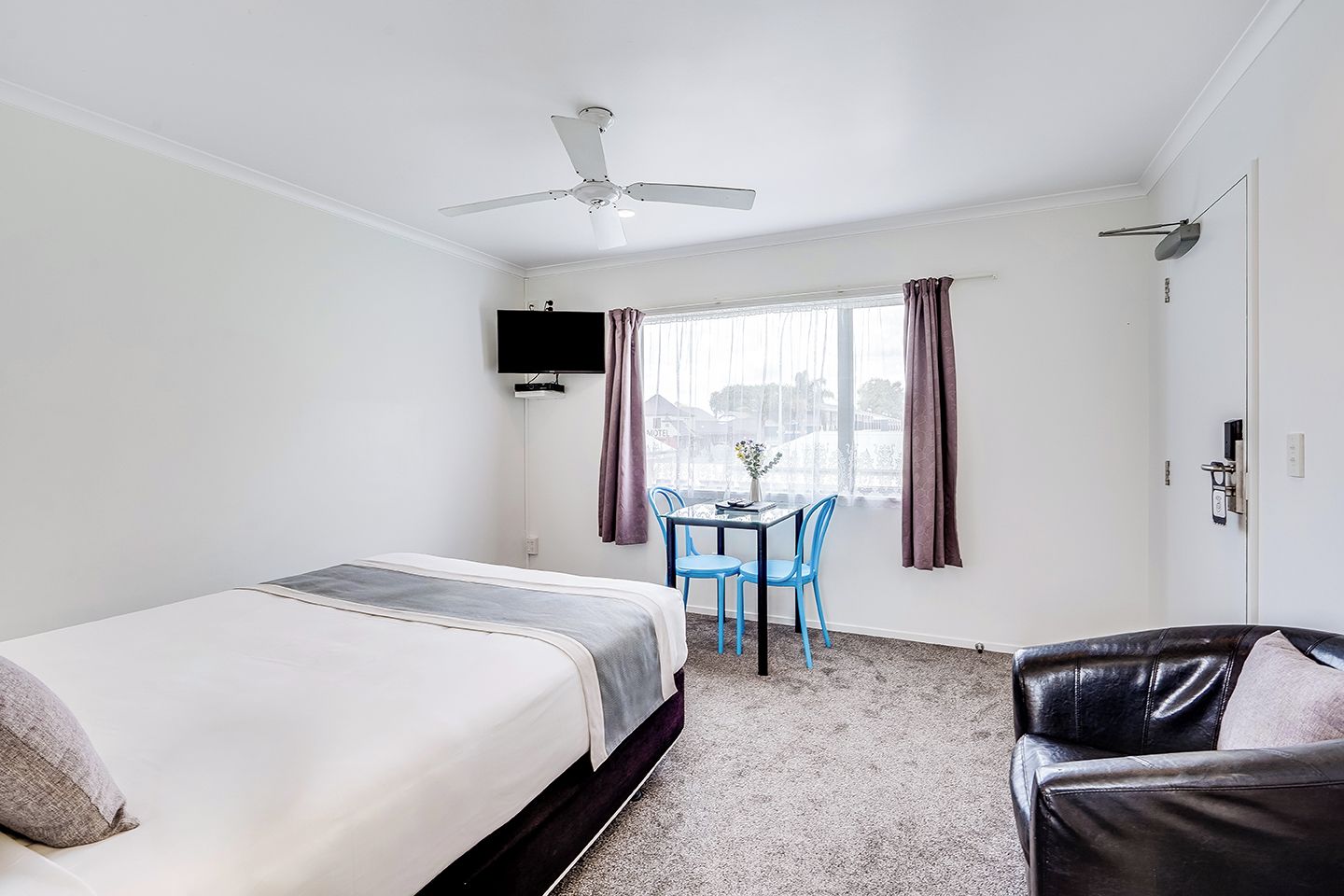 Una habitación de hotel con una cama, un escritorio con sillas, un televisor y un ventilador de techo.