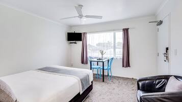 Una habitación de hotel con una cama, un escritorio con sillas, un televisor y un ventilador de techo.