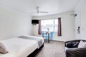 A hotel room with a bed, a desk with chairs, a television, and a ceiling fan. - Hamilton Settlers Motor Lodge (Hamilton)