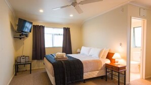 A bedroom with a bed, a ceiling fan, a TV mounted on the wall, a bedside table with a lamp, and a window with curtains. - Hamilton Settlers Motor Lodge (Hamilton)