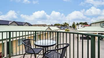 Een balkon met een ronde tafel en twee stoelen, met uitzicht op een straat met gebouwen.