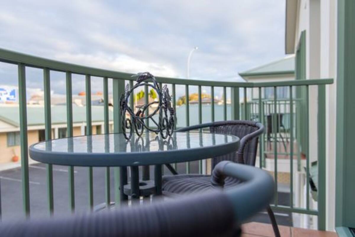A balcony with a round glass table and two wicker chairs.