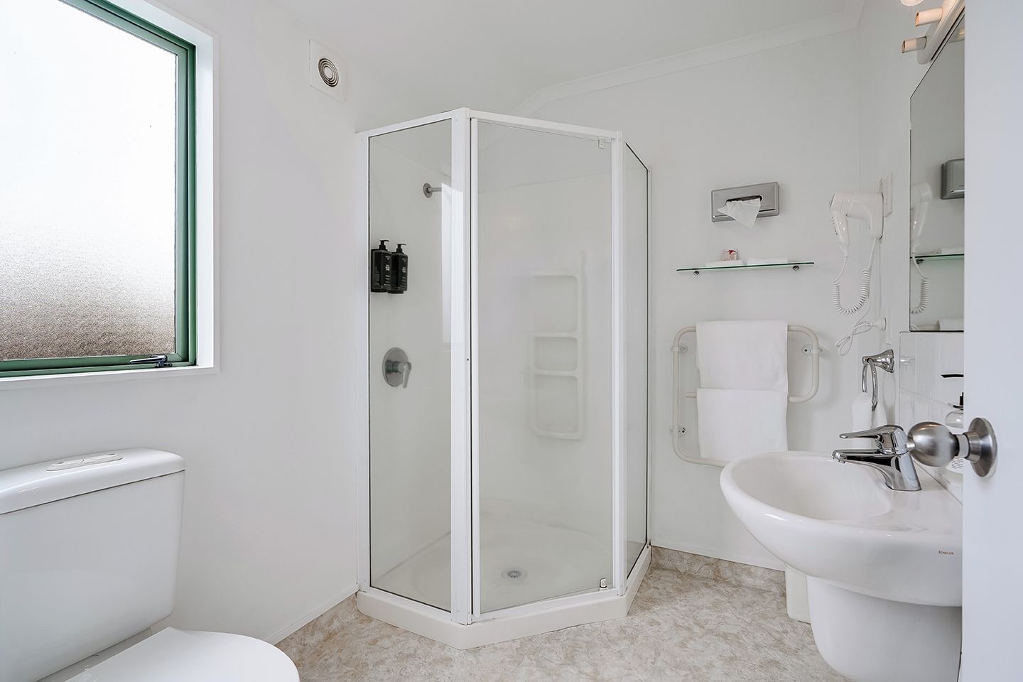 A modern bathroom with a glass-enclosed shower, a toilet, a sink, and a window.