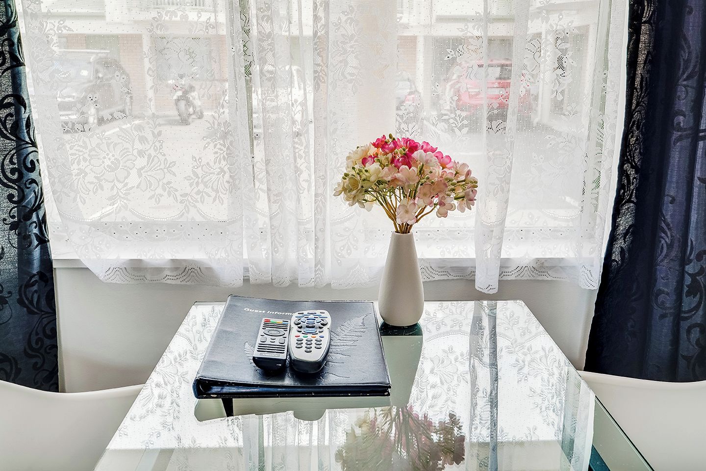 Una habitación con una mesa de vidrio, un jarrón con flores y un control remoto.