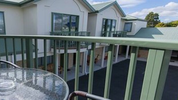 A balcony with a glass table and chairs, overlooking a residential area with houses. - Hamilton Settlers Motor Lodge (Hamilton)