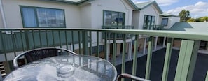 A balcony with a glass table and chairs, overlooking a residential area with houses.