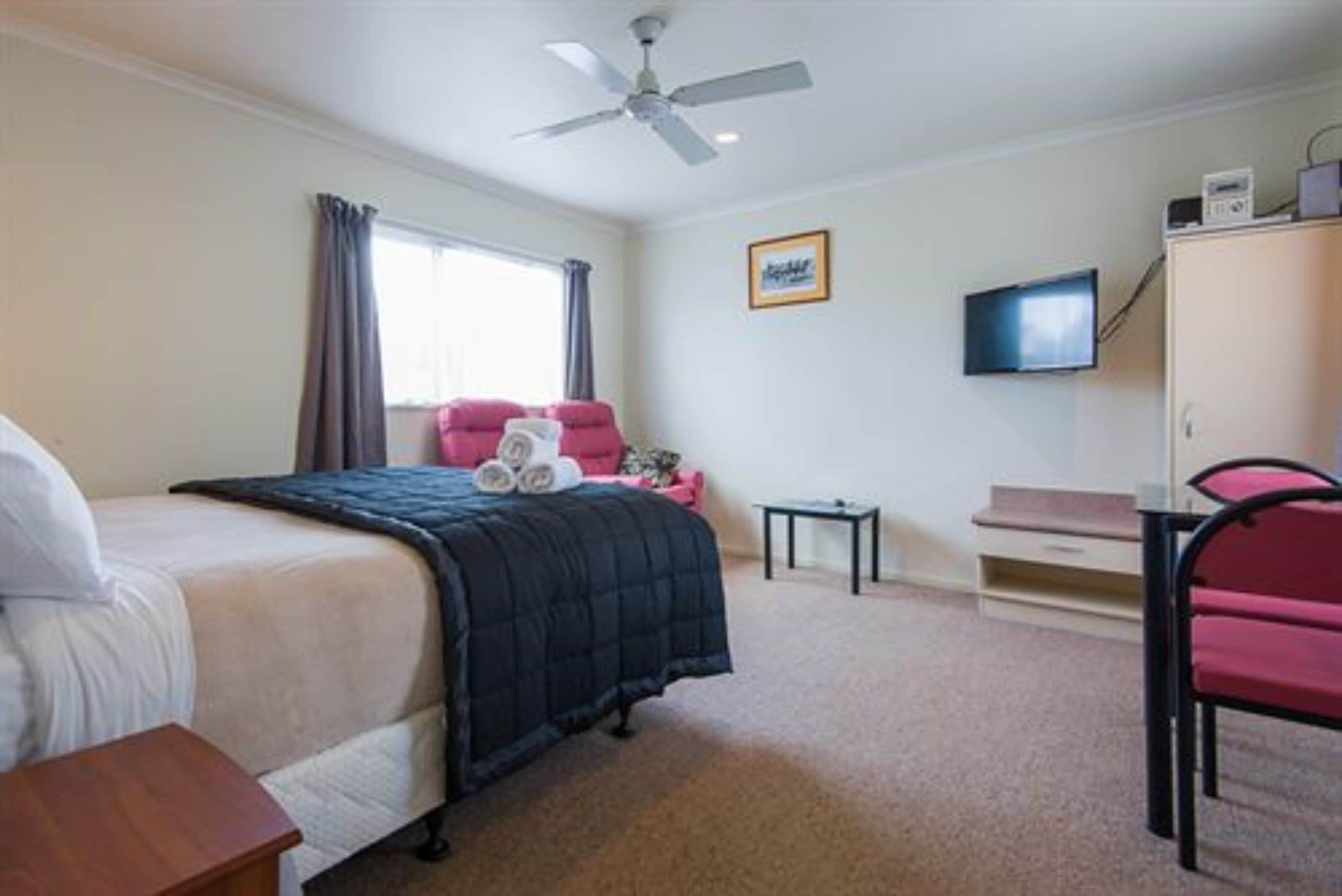 A bedroom with a bed, a desk, a chair, a television, and a ceiling fan.