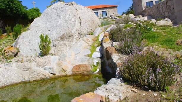 A natural landscape with a rock formation, a small water feature, and buildings in the background. - Lousada Country Hotel (Lousada)