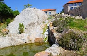 A natural landscape with a rock formation, a small water feature, and buildings in the background. - Lousada Country Hotel (Lousada)