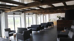 A modern lounge area with dark sofas and chairs, a wooden reception desk, and large windows offering a view of the outdoors. - Lousada Country Hotel (Lousada)