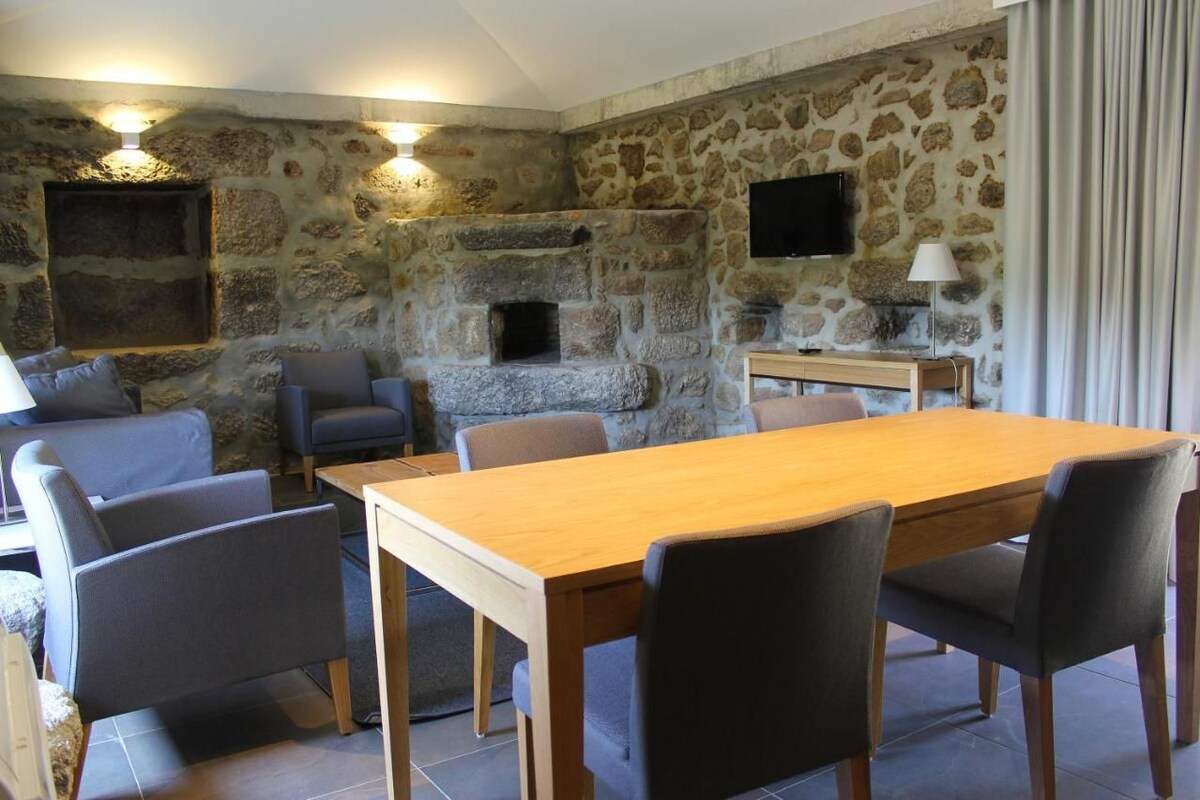 Une pièce aux murs de pierre, dotée d’une cheminée, d’un téléviseur fixé au mur et d’une table à manger avec des chaises.