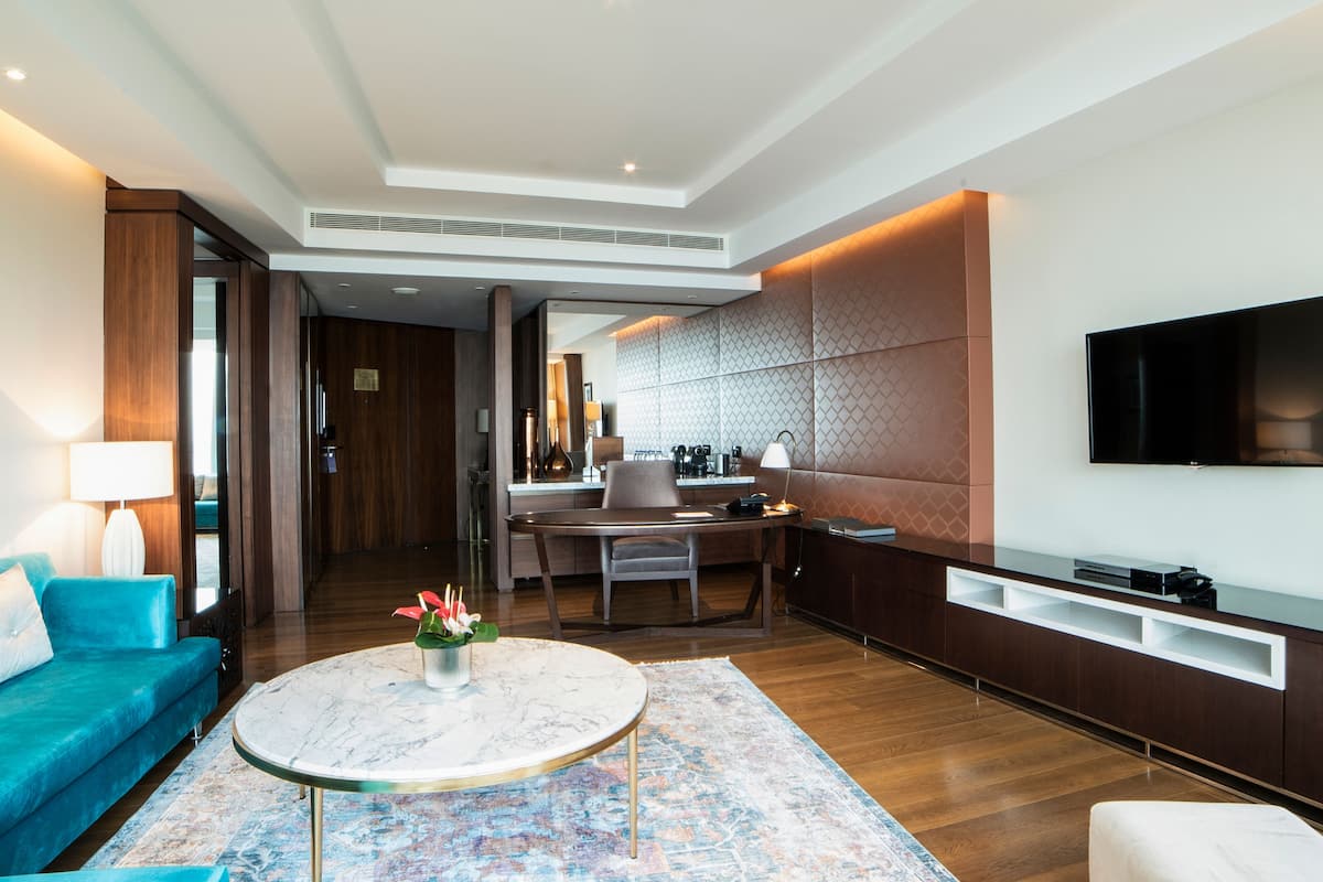 Habitació d'hotel moderna amb sofà, taula de centre rodona, zona de menjador amb taula i cadires, taulell de cuina i televisió penjada.