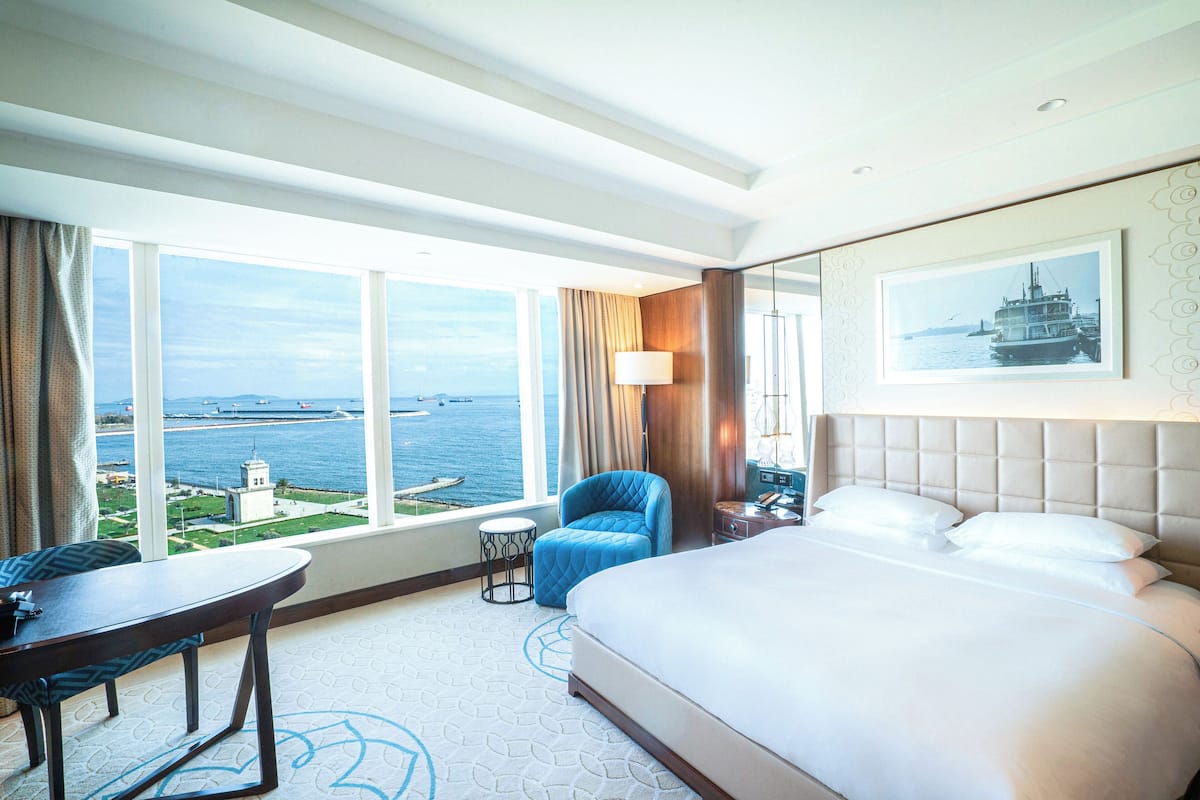 Una habitació d'hotel amb un llit gran, una taula, una cadira i vistes al mar.