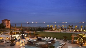 Un espace piscine sur le toit, avec des chaises longues, une petite piscine et une vue sur la mer, où l'on peut observer les navires la nuit.