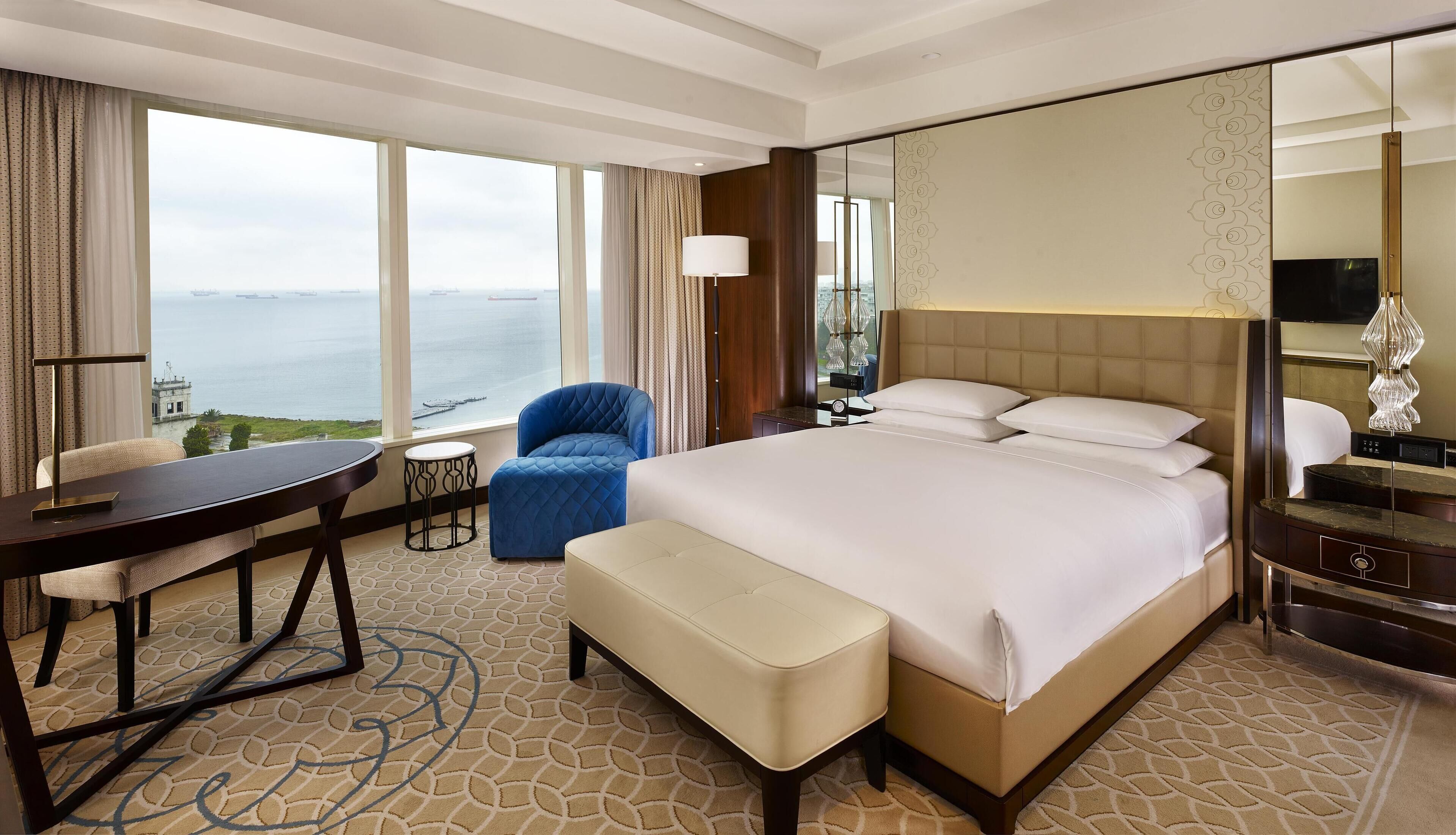 A hotel room with a large bed, a desk, a chair, and a view of the sea.