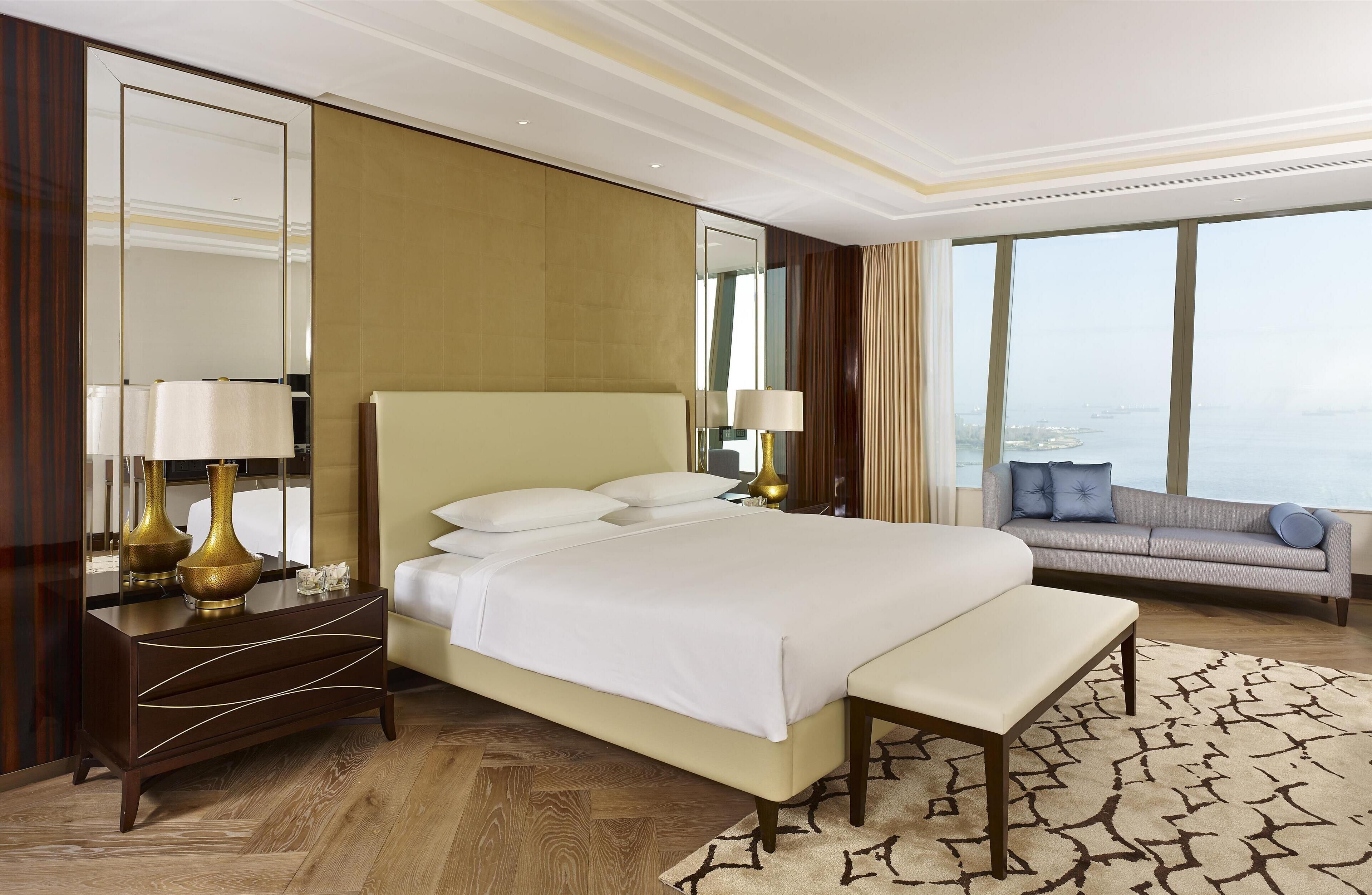 A hotel room with a large bed, bedside tables, a sofa, and a view of the city.