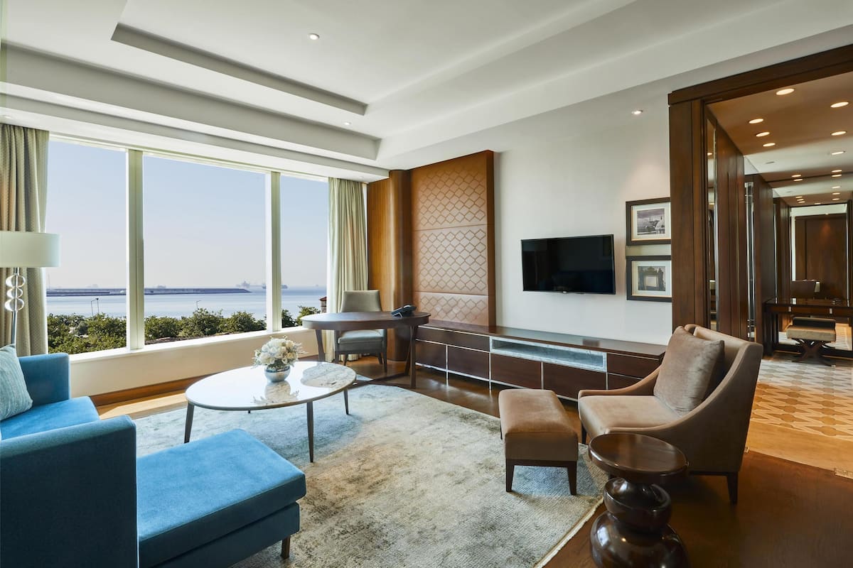 Habitació d'hotel moderna amb una finestra gran que ofereix una vista a la ciutat, un televisor de pantalla plana fixat a la paret i una zona de seients amb un sofà i butaques.