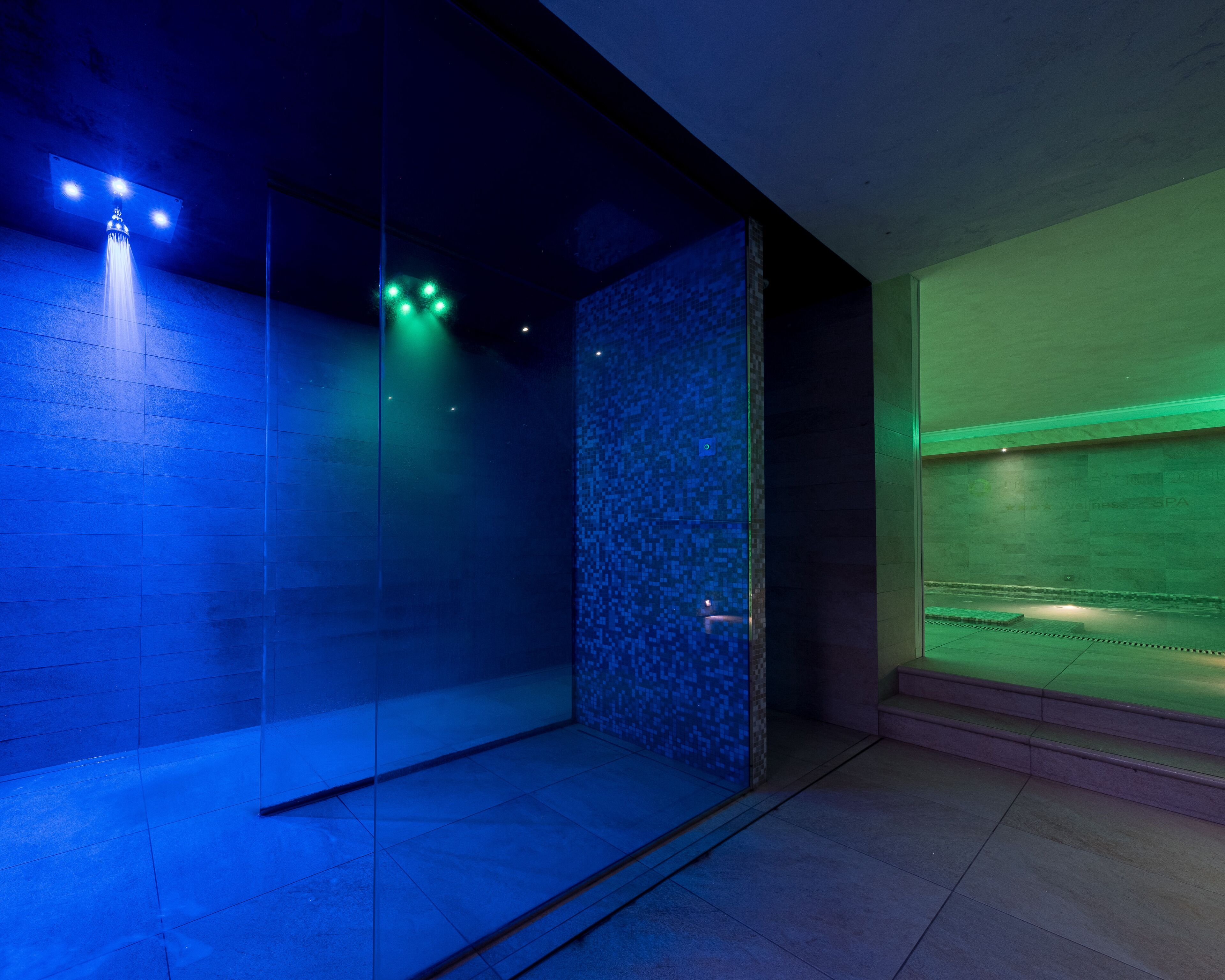 Um banheiro moderno com box de vidro, piso revestido e parede com iluminação verde.