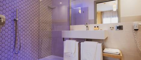 Une salle de bain moderne avec une douche à parois de verre, un meuble-lavabo avec un miroir et une étagère en bois où sont rangées des serviettes et des articles de toilette.