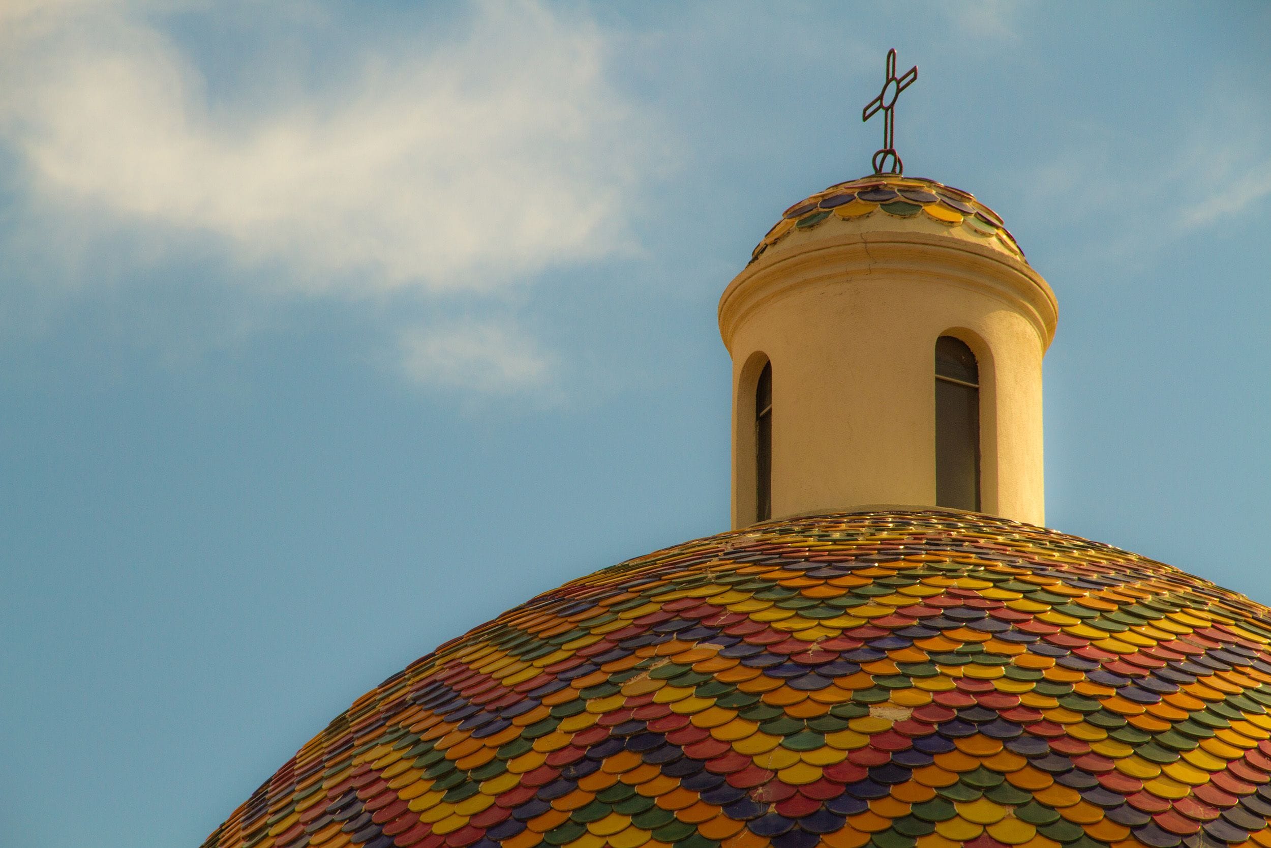 Un bâtiment surmonté d’un dôme aux tuiles colorées et d’une croix.