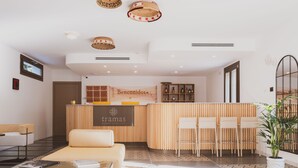 En hotellobby med en receptionsdisk i trä, en soffa och ett soffbord. I taket hänger lampor av rotting, och i ett hörn står en krukväxt.