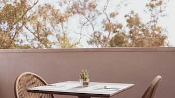 A table with a cactus on it, surrounded by wicker chairs, with a view of trees in the background.
