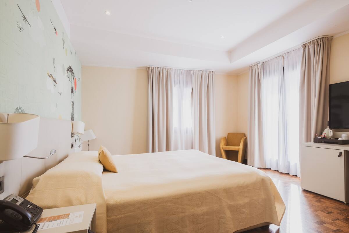 A hotel room with a bed, a desk with a telephone, a chair, a television, and curtains.