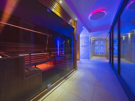 A modern hotel corridor with glass doors, a reception desk, and a seating area with a red-lit bench.