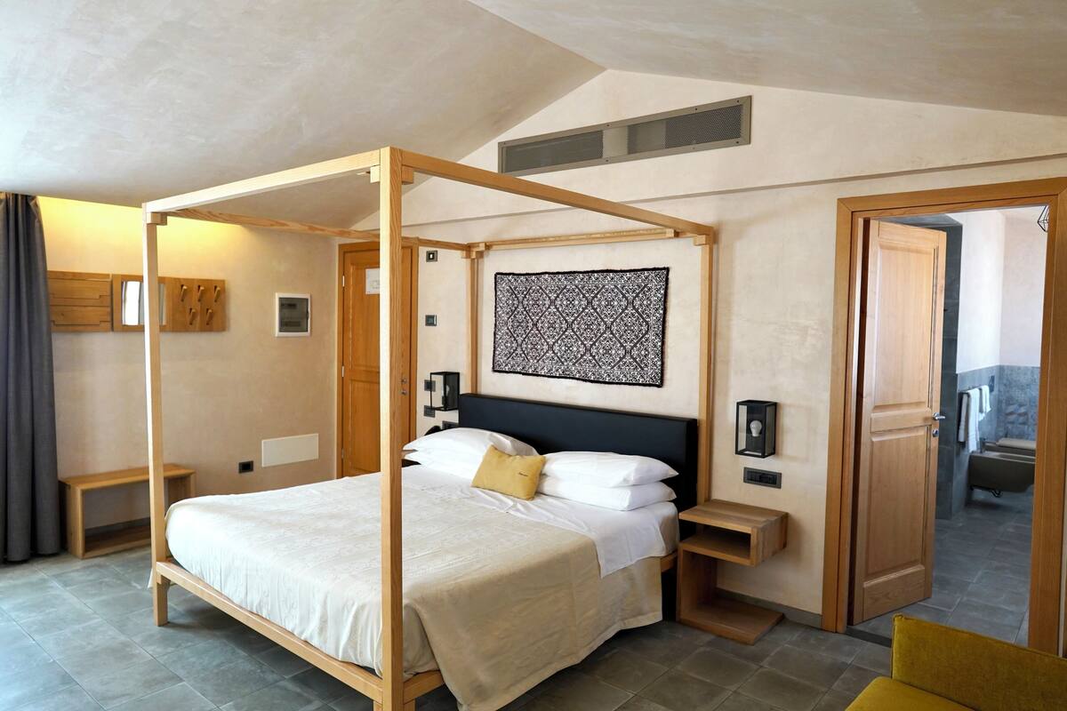 A four-poster bed with a headboard, bedside tables, a bench, and a wall-mounted artwork.