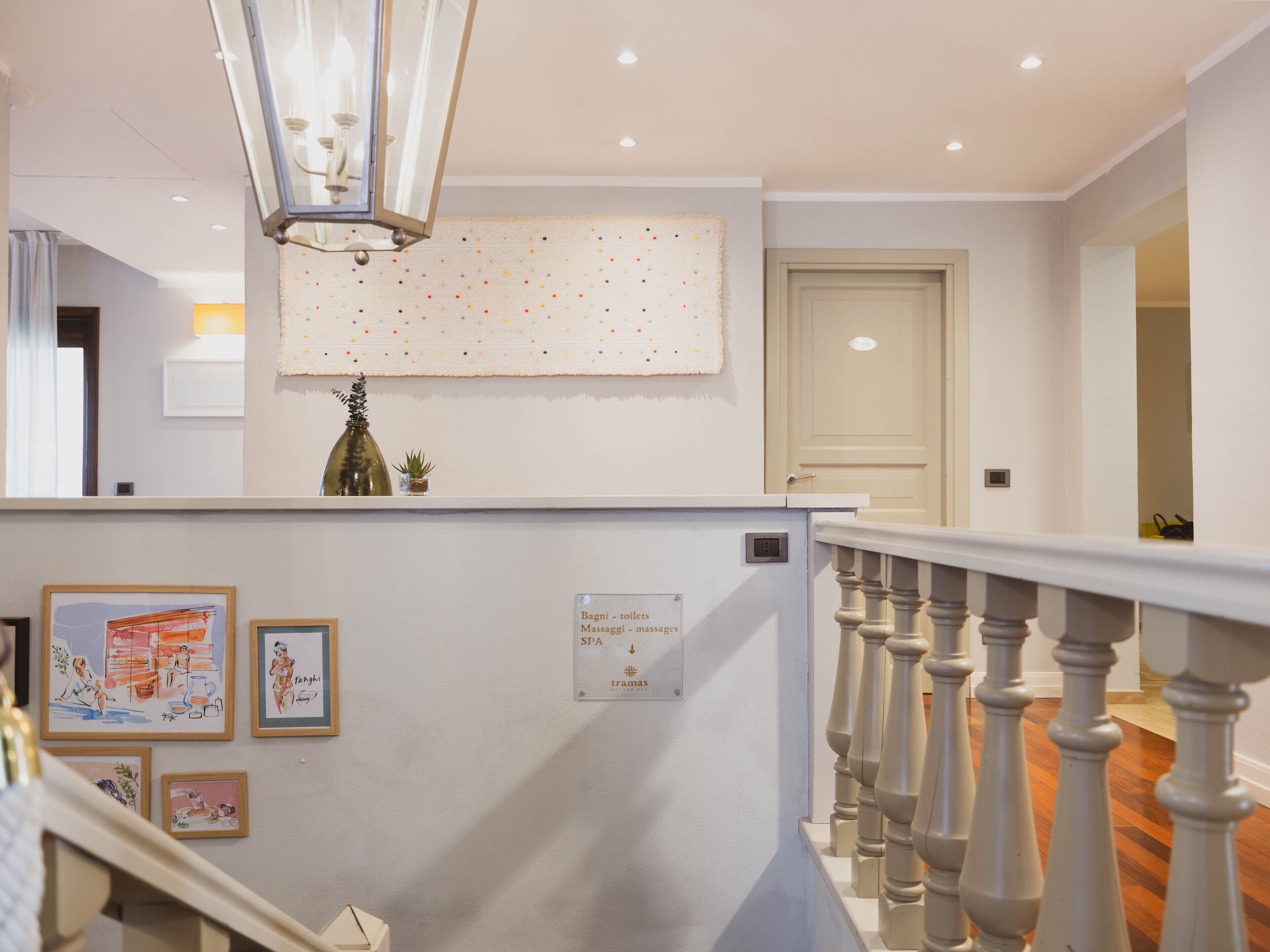A hotel lobby with a staircase, a chandelier, a wall with framed artwork, and a sign indicating spa services.