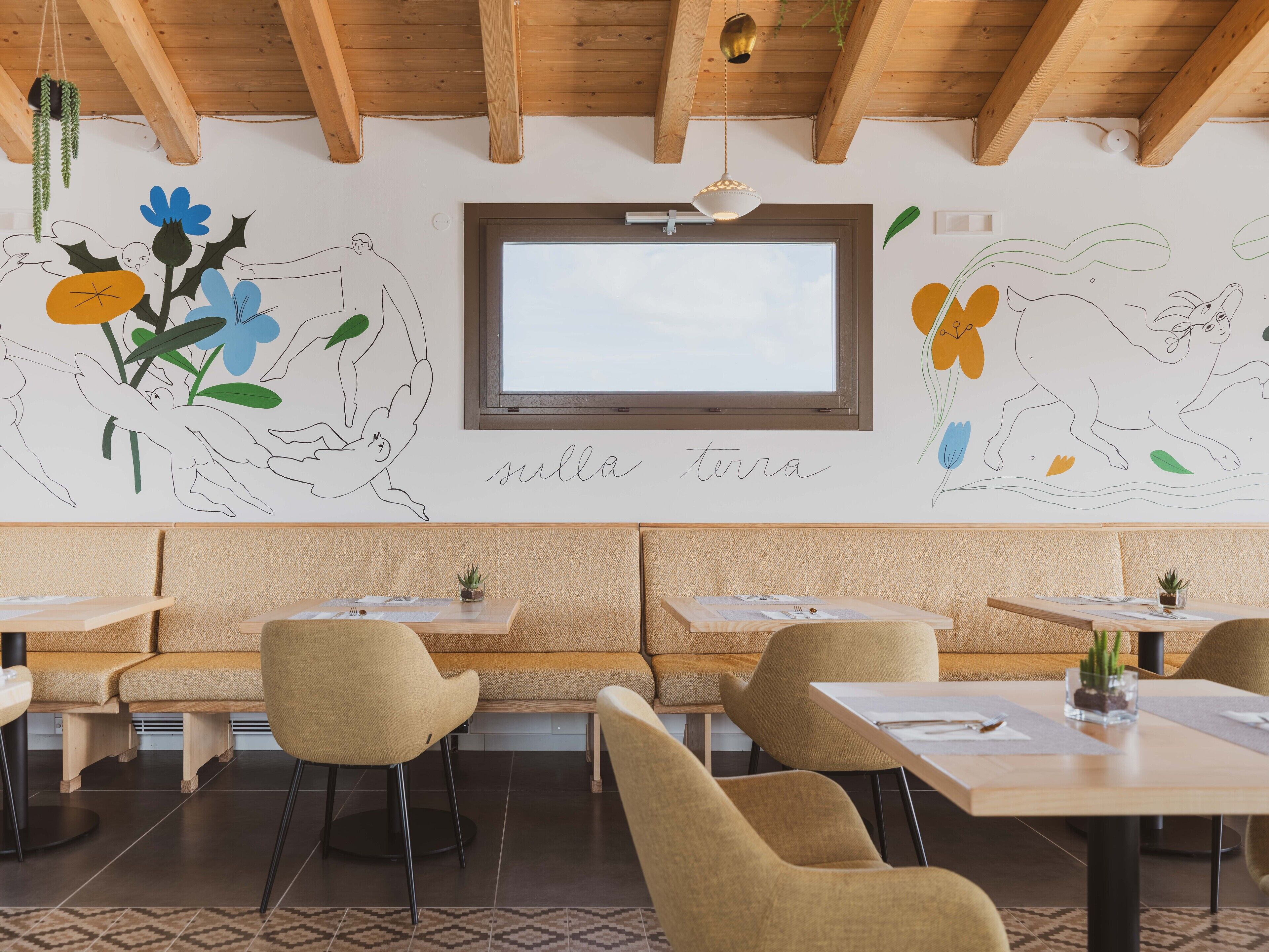 Un restaurante con vigas de madera en el techo, un ventanal grande y un mural con arte abstracto y la frase "sulla terra".