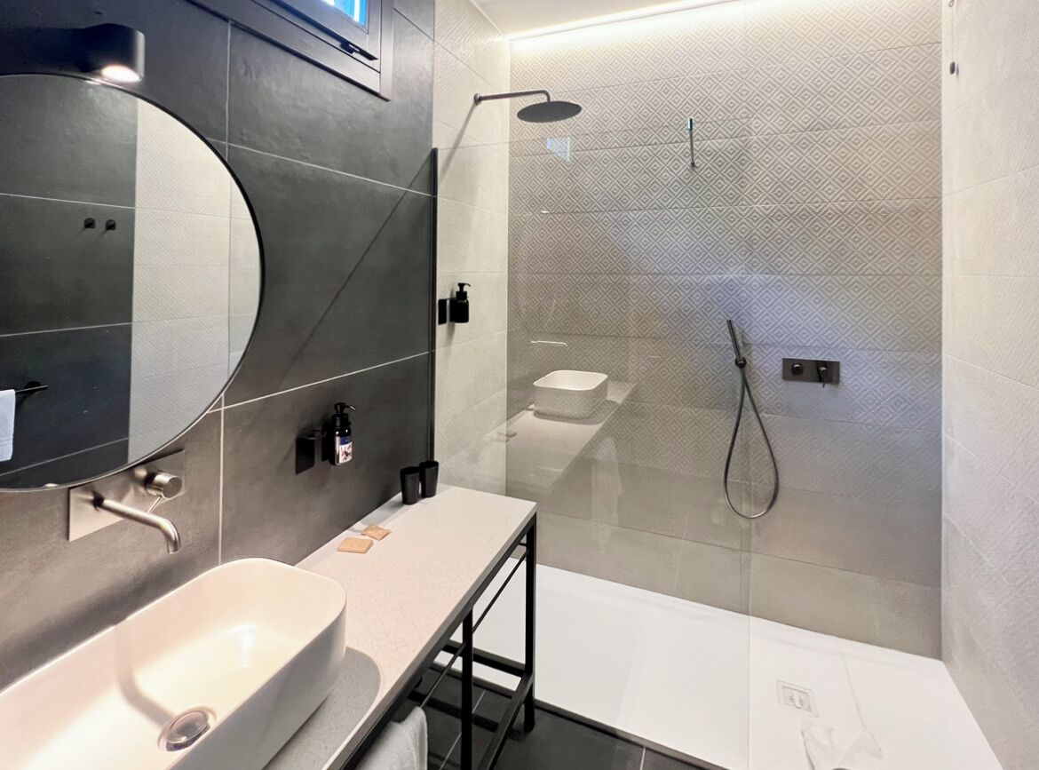 Een moderne badkamer met een grote spiegel, een witte wastafel, een douchecabine van glas en een witte badkamerkast.