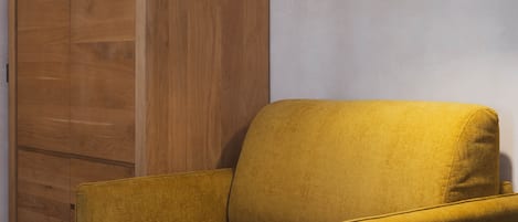 A mustard-colored sofa in a room with wooden paneling and a wall-mounted lamp.