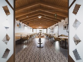 A spacious dining area with wooden ceiling beams, patterned floor tiles, and modern furniture.