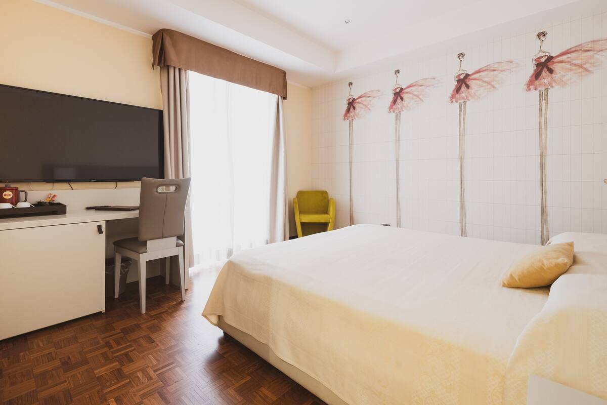 A hotel room with a bed, a desk, a chair, a television, and a wall with decorative elements.
