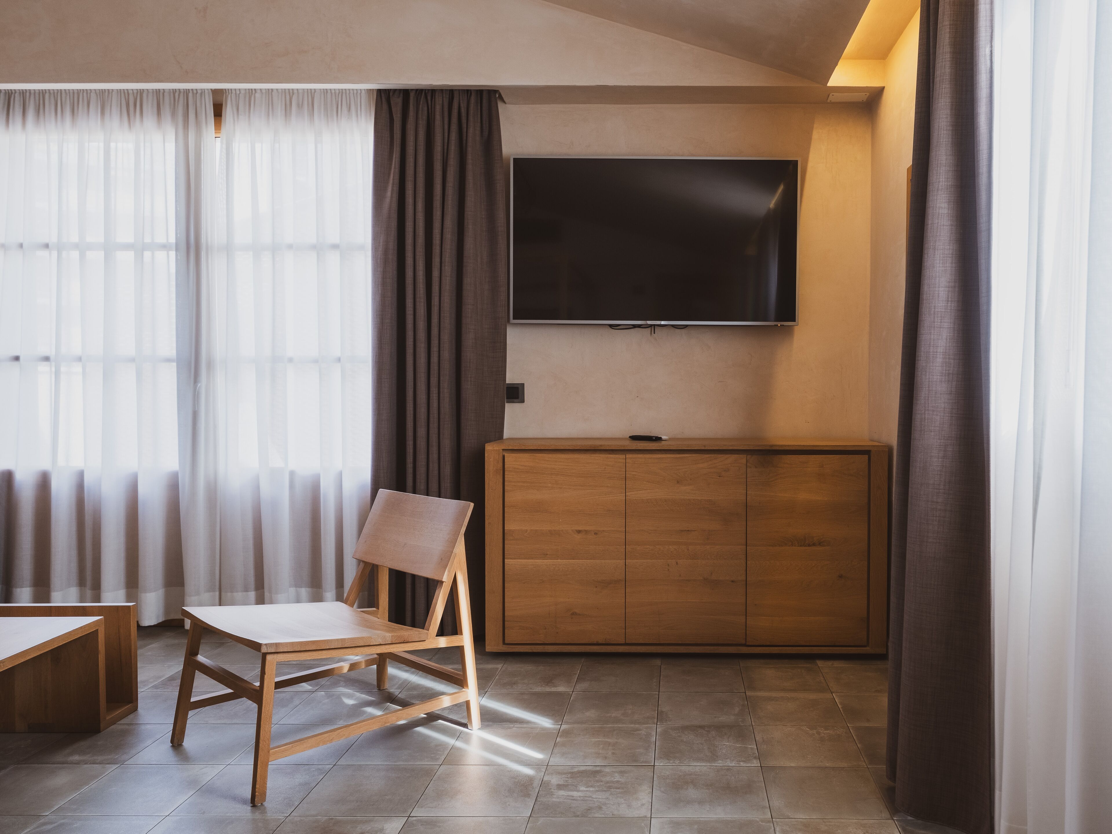 Una sala moderna con un aparador de madera, un televisor de pantalla plana montado en la pared y una silla de madera.