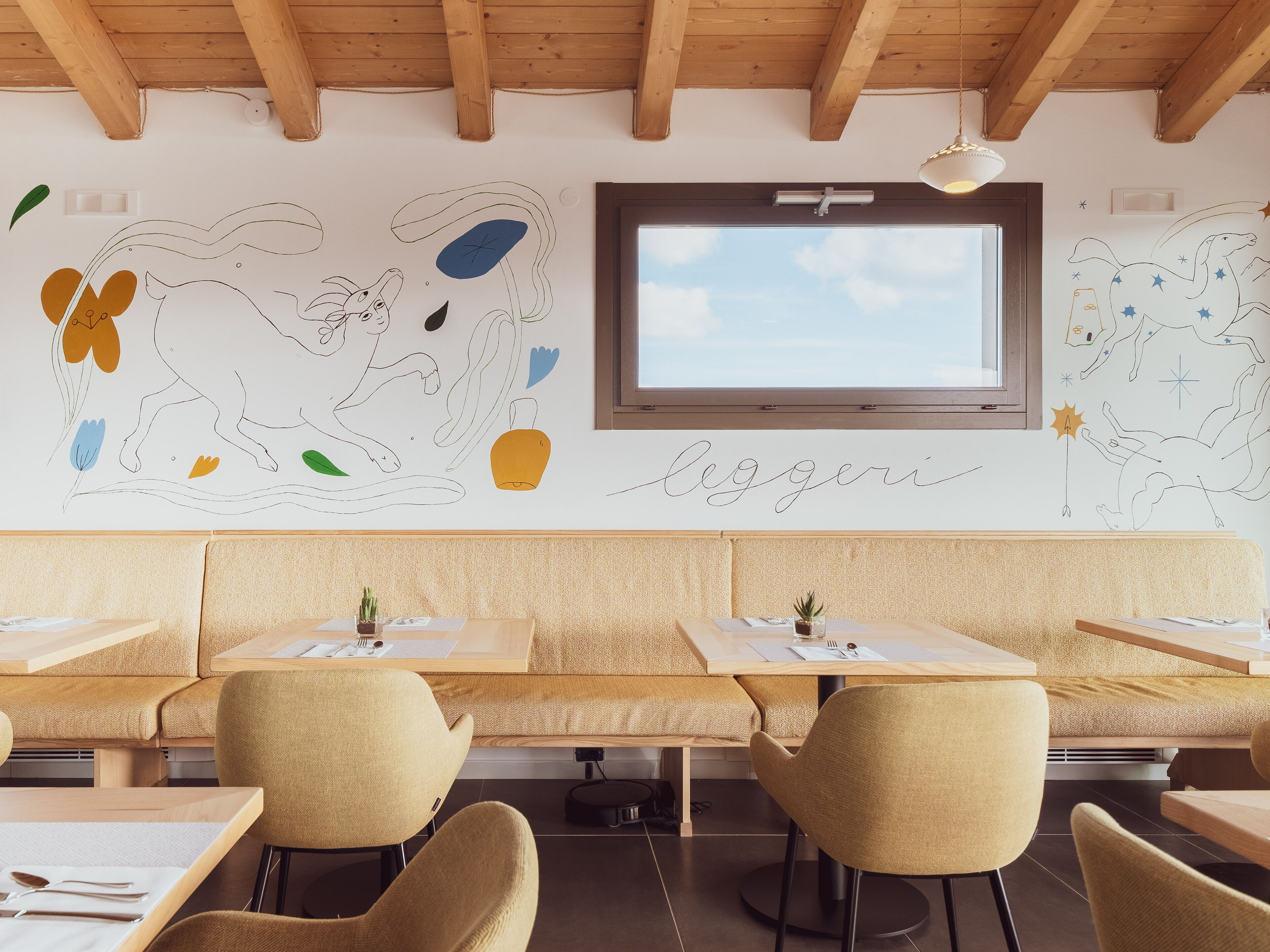 Un comedor moderno con mesas y sillas de madera, un ventanal grande y arte abstracto en la pared.