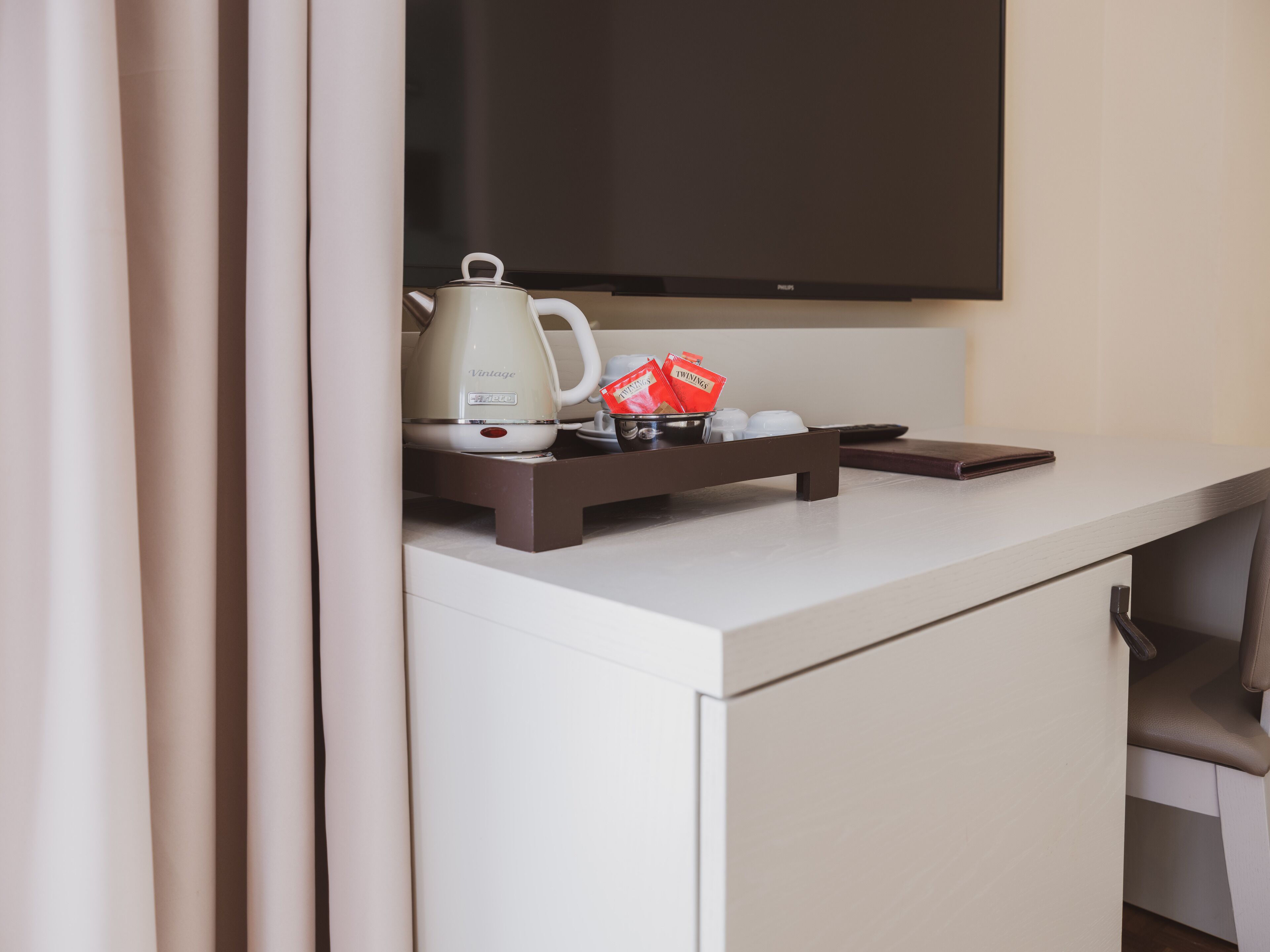 A white desk with a kettle, a tray with a red item, and a remote control.