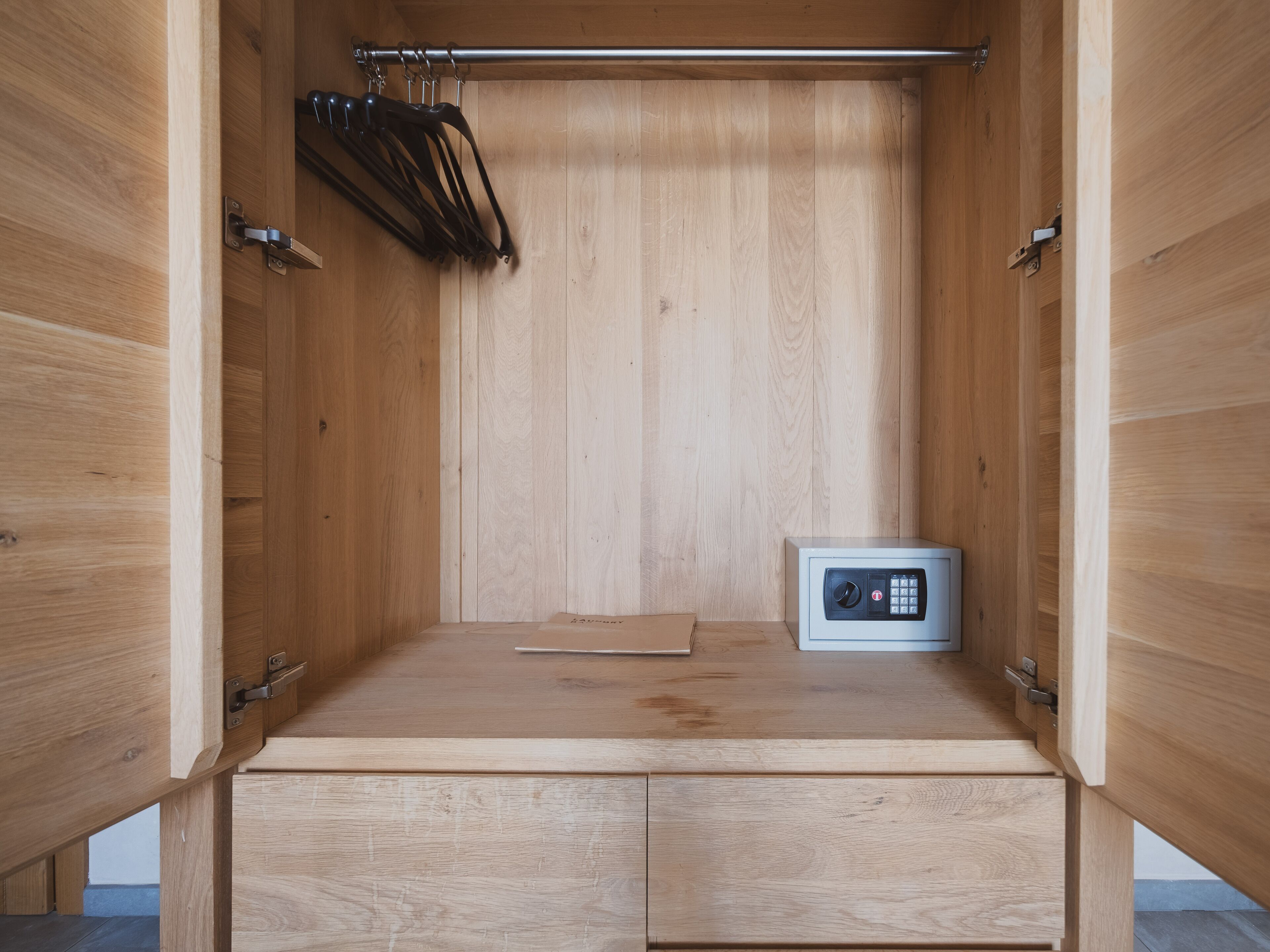 A wooden cabinet with a built-in safe, a hanging rack, and a flat surface.