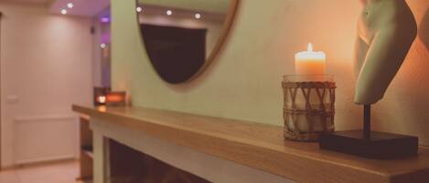 A wooden console table with a lit candle, a decorative glass, and a sculpture.