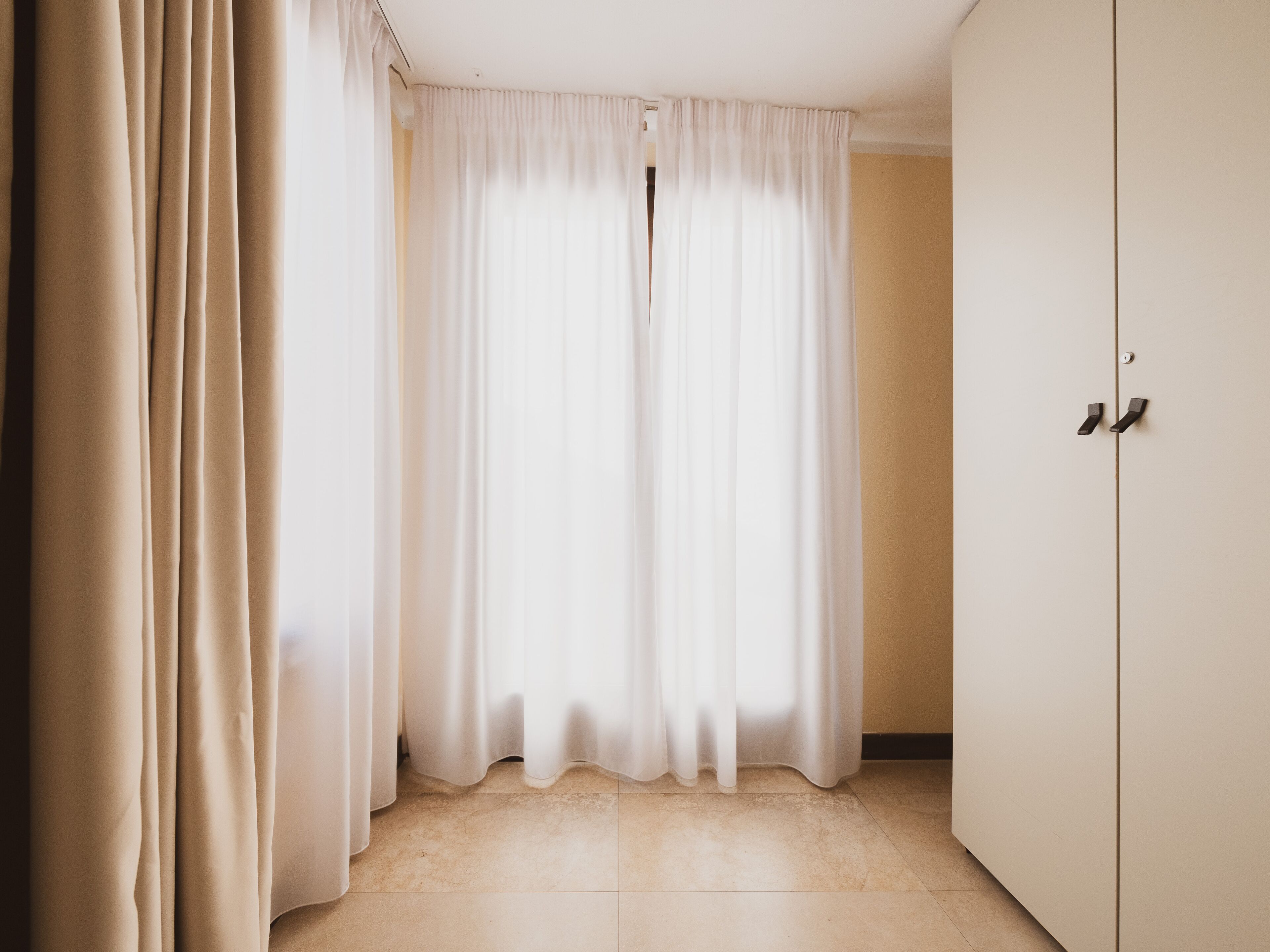 Una habitación con cortinas color beige, suelo de baldosas y una puerta con picaporte.