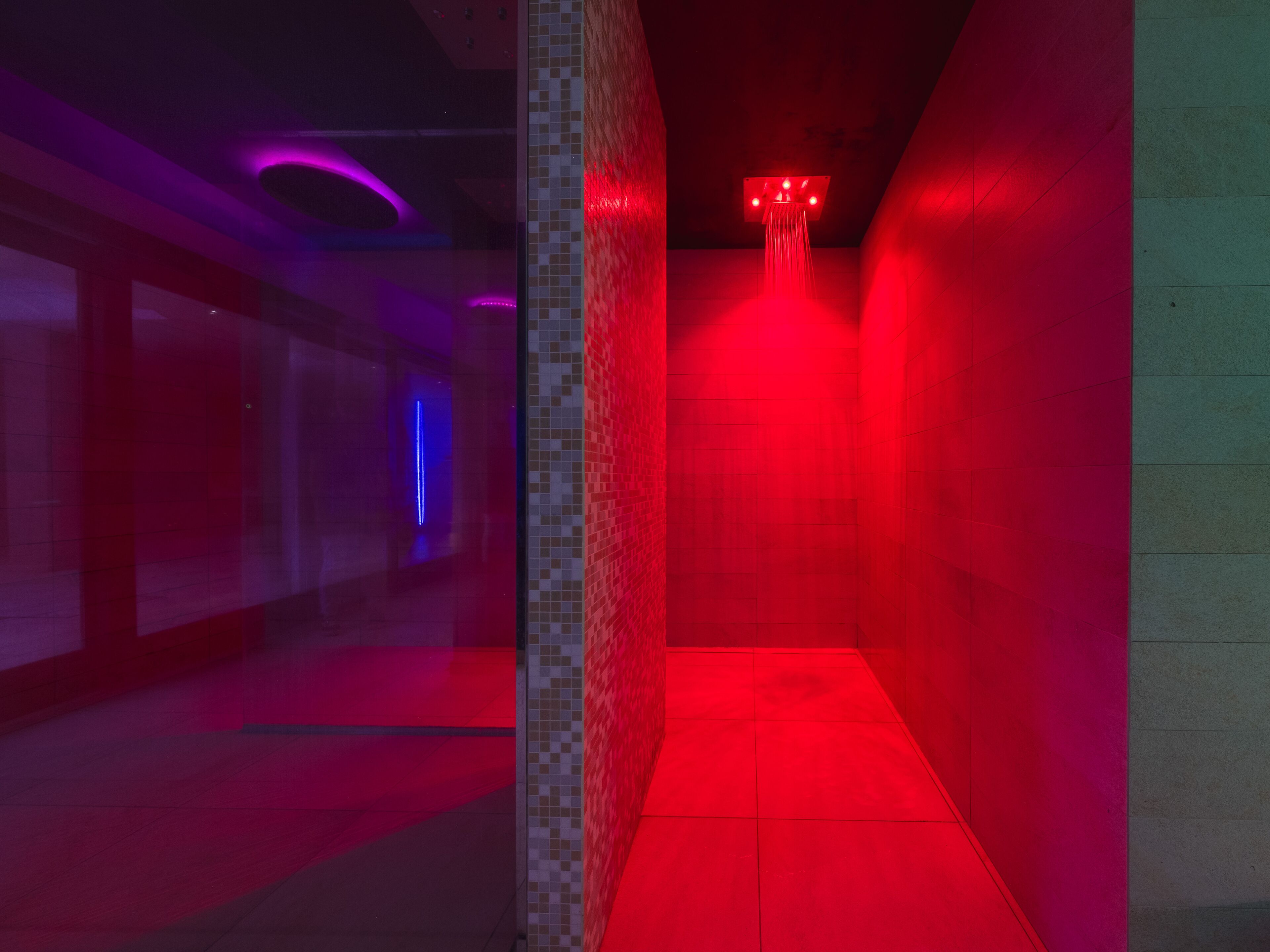 A hallway with a red-lit shower area and a blue-lit passageway.
