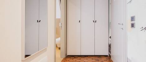 A hallway with a wooden parquet floor, white walls, and a white wardrobe with two doors.