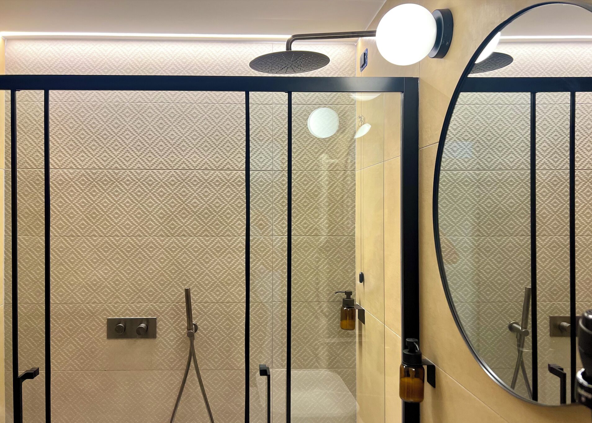 A modern bathroom with a glass shower enclosure, a round mirror, and a wall-mounted towel rack.