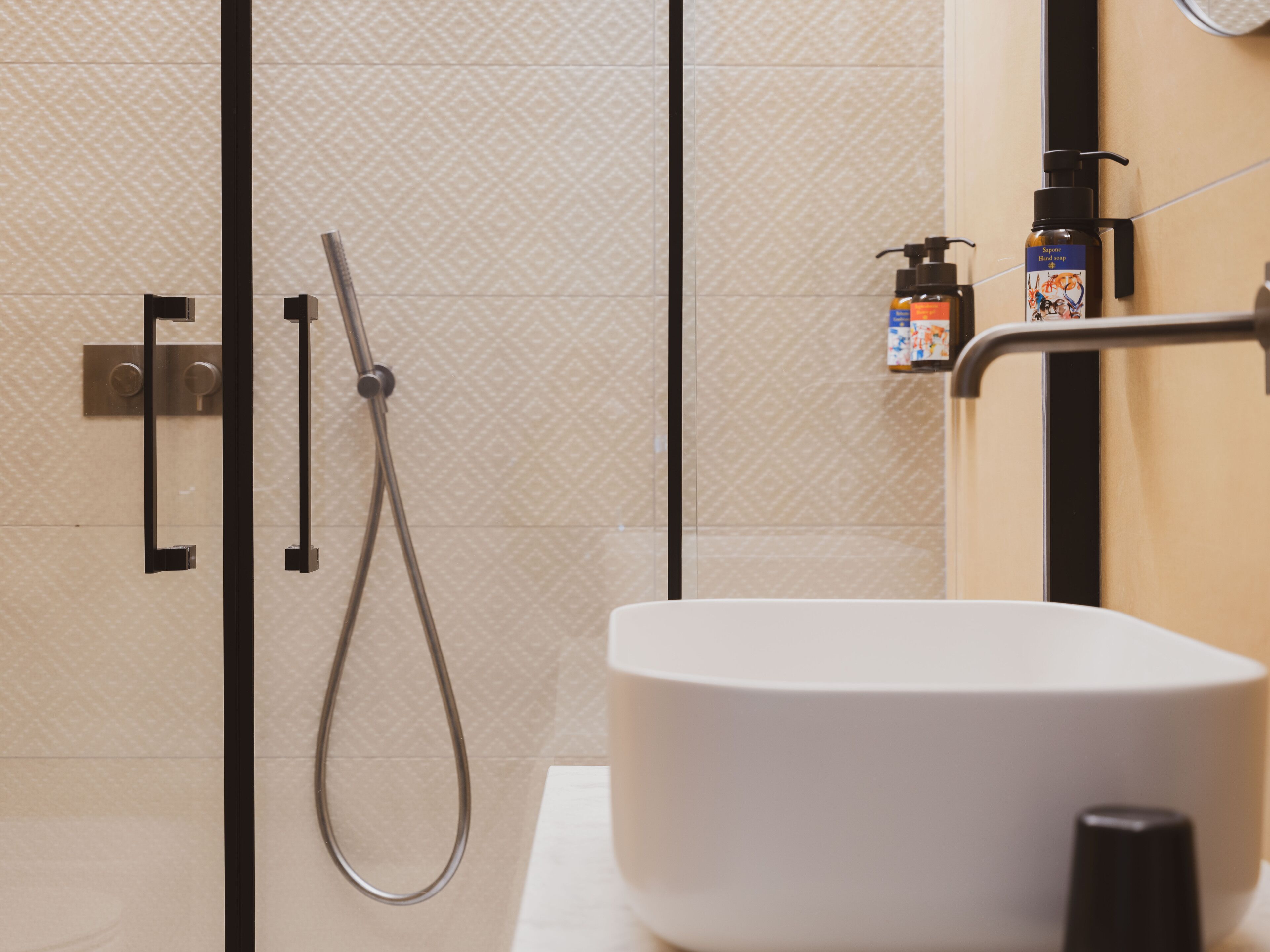 A modern bathroom with a shower, a white sink, and a soap dispenser on the wall.