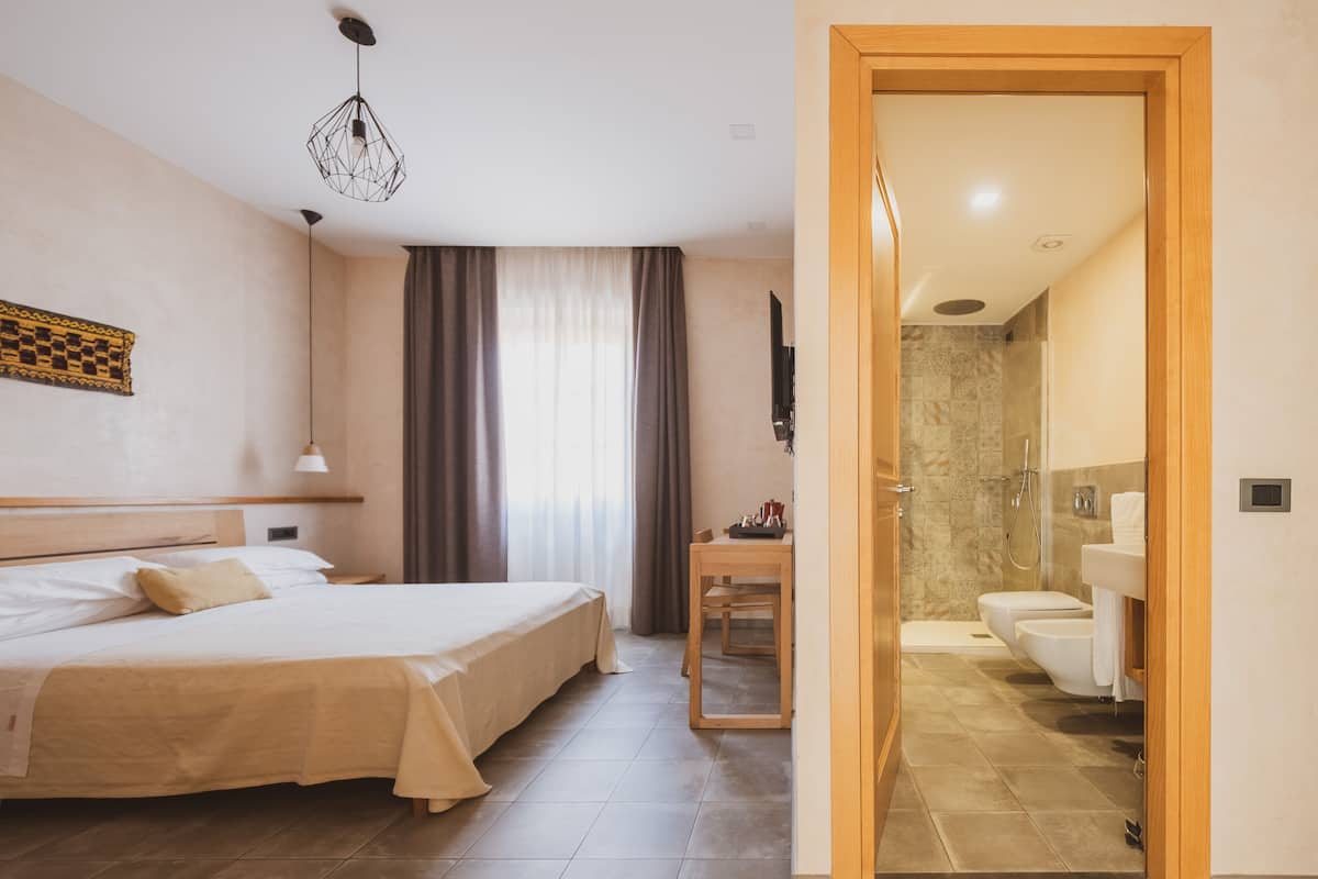 A hotel room with a bed, a desk, a chair, a bathroom with a toilet and shower, and a wooden door.